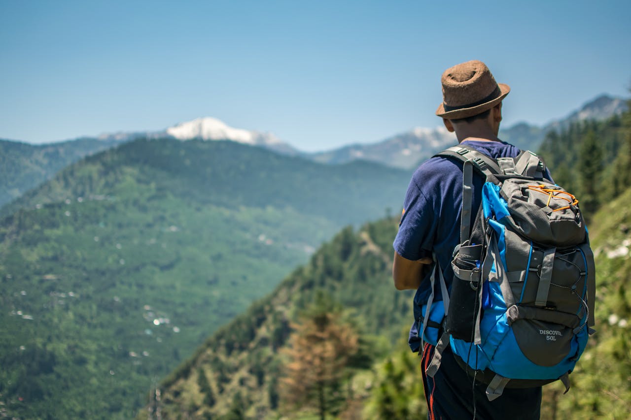 Man with backpack hiking among green mountains under clear blue sky.